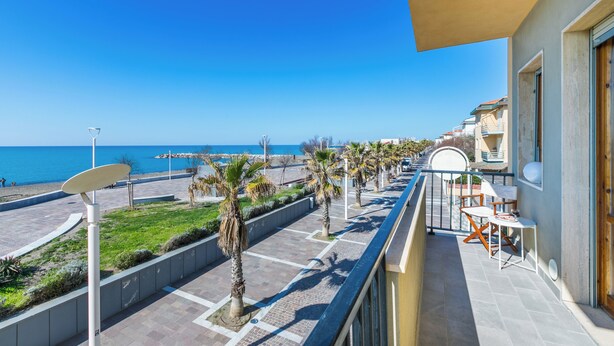 Een balkon met uitzicht op zee, een palmboom en een stoel.