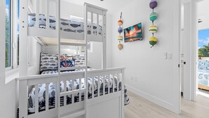 A room with a bunk bed, a ceiling fan, a wall-mounted TV, and a view of the outdoors.