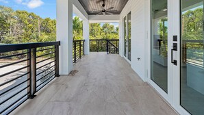 A covered outdoor balcony with a ceiling fan, glass doors, and a view of greenery.