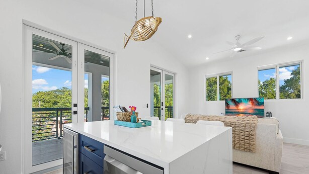 A modern kitchen with a large island, sliding glass doors to a balcony, and a dining area with a sofa and TV.