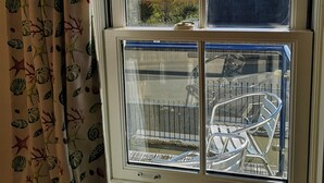 Una ventana con vista a un paisaje costero, que incluye una silla de metal y una concha decorativa.