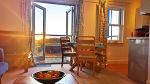 Una habitación con una mesa de comedor, sillas, un cuenco de fruta y vistas a través de una puerta abierta.
