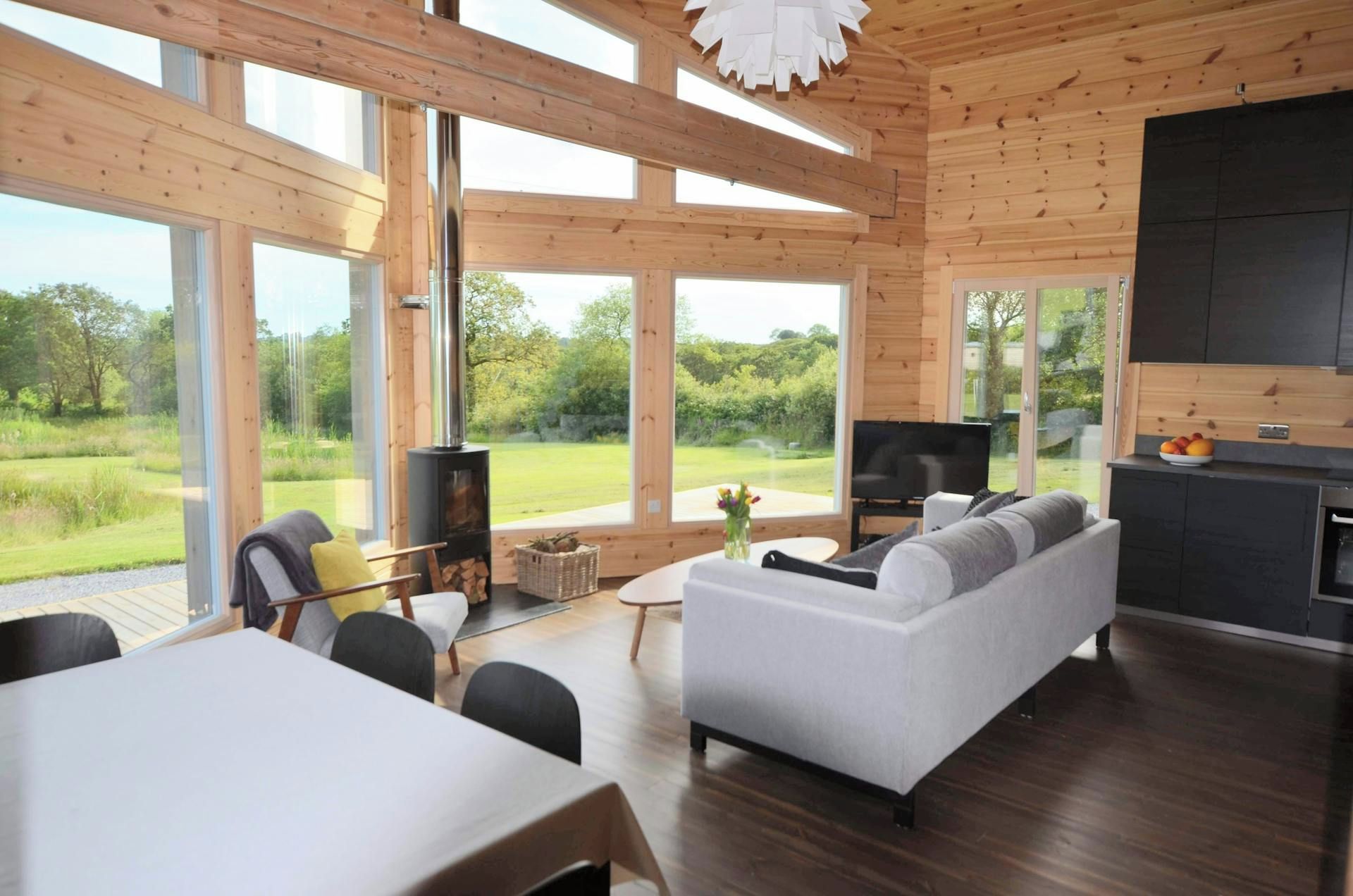 Un interior moderno con sofá, mesa de comedor y televisor. Amplias ventanas ofrecen vistas al exterior.