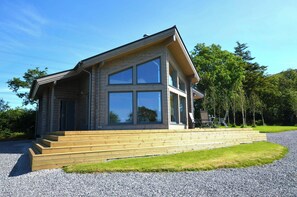 A modern two-story house with a large front window and a wooden deck. - Ty Log, Llansteffan - Two Bedroom Cottage, Sleeps 4 (Llangain)