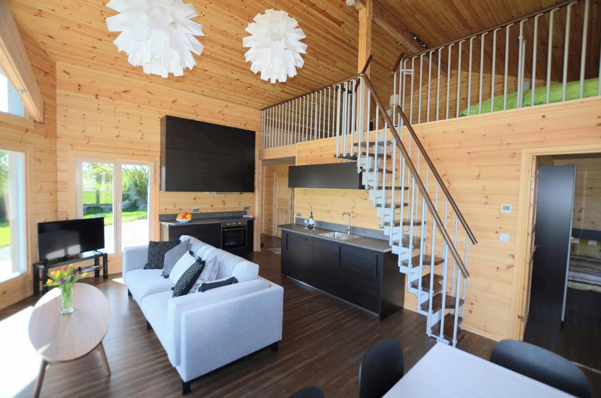 Ein modernes Blockhaus-Interieur mit Wohnbereich, Sofa, Esstisch, Küche und einer Wendeltreppe.