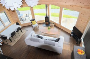 A cozy interior with a sofa, a dining table, chairs, a fireplace, and large windows offering a view of the outdoors. - Ty Log, Llansteffan - Two Bedroom Cottage, Sleeps 4 (Llangain)