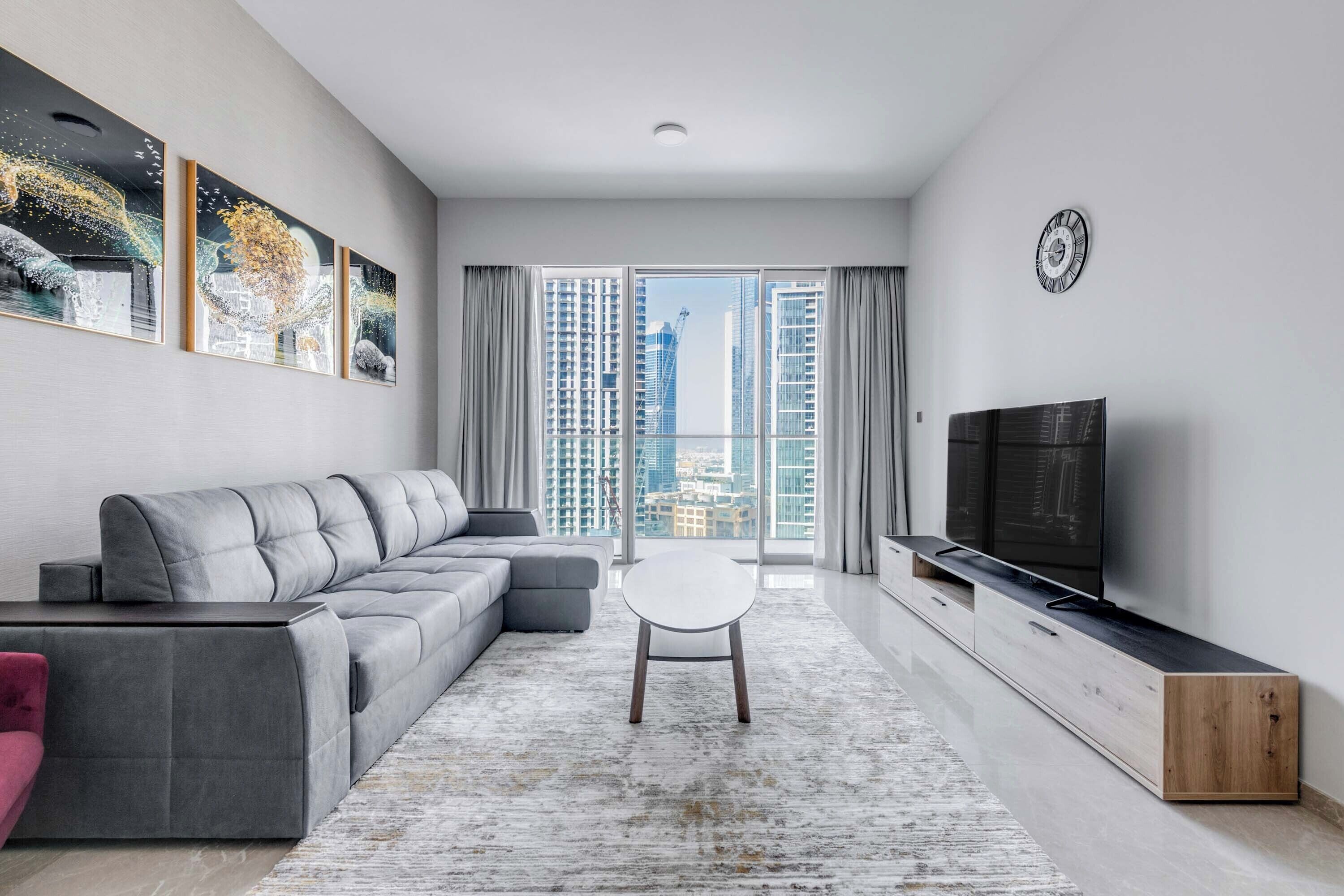 A modern living room with a grey sectional sofa, a white coffee table, and a TV on a wooden stand.