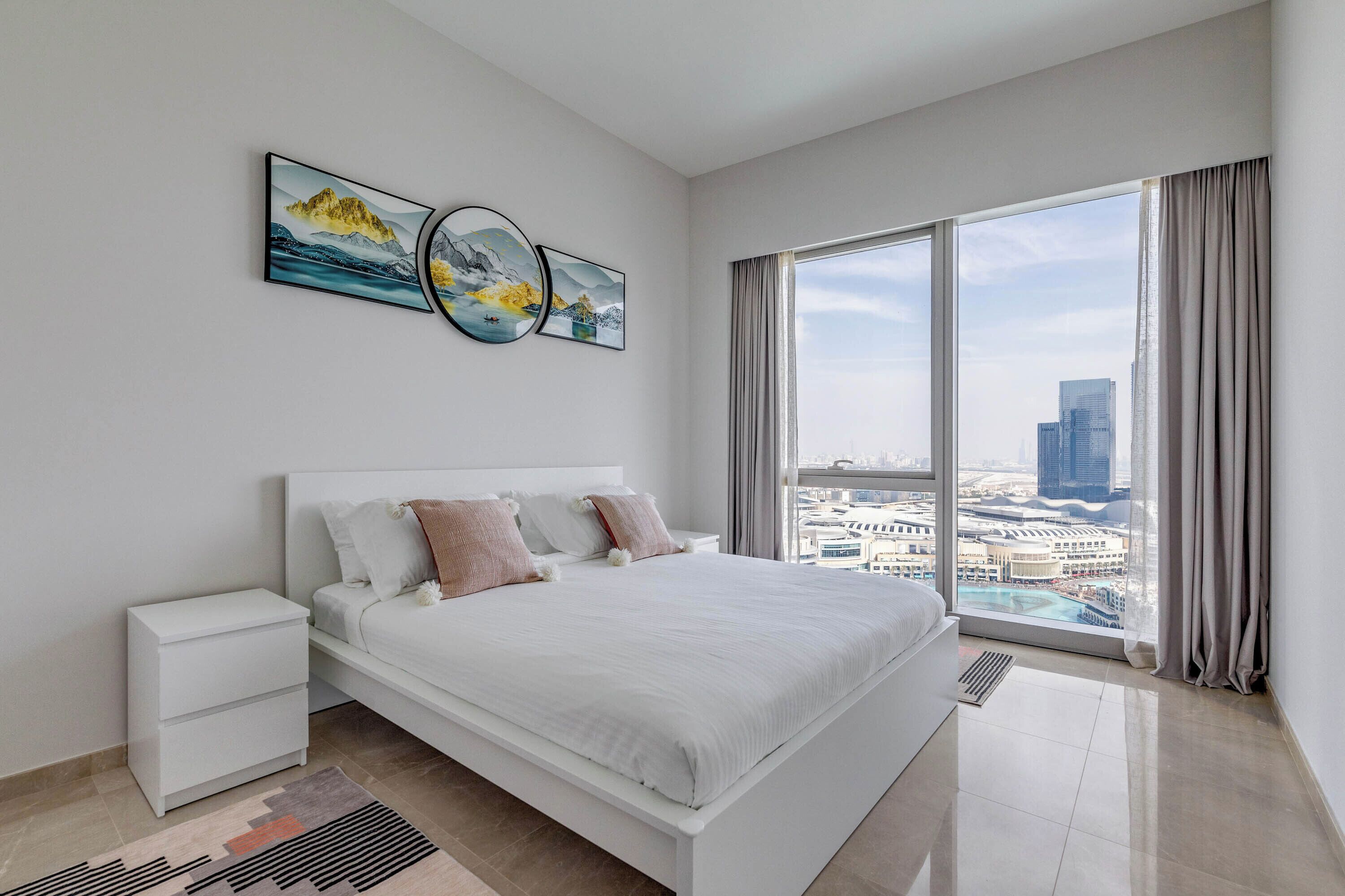 Een moderne slaapkamer met een groot bed, een nachtkastje en een stadsgezicht door grote ramen.