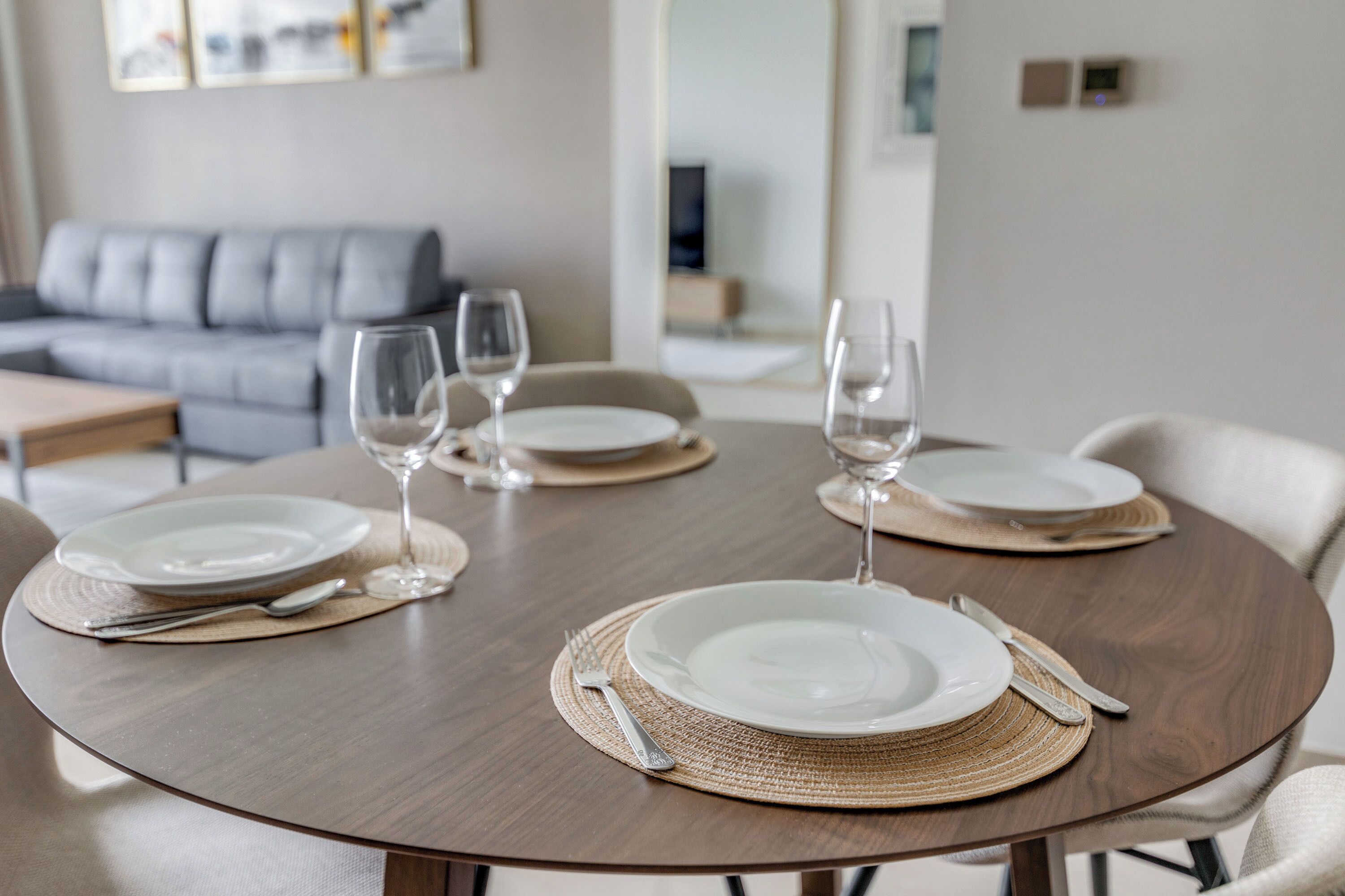 Een eettafel gedekt met borden, bestek en wijnglazen, met een bank en een televisie op de achtergrond.