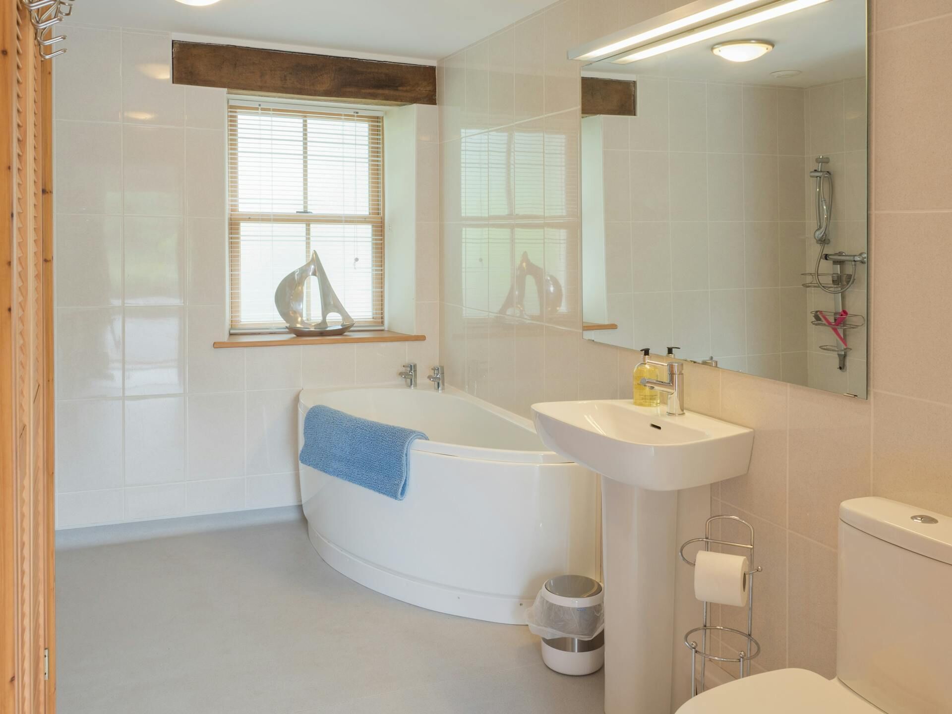 A modern bathroom with a freestanding bathtub, a sink, a toilet, and a window with blinds.