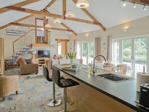 A spacious kitchen with a central island, a dining area with chairs, a sofa, and a TV in the living room.