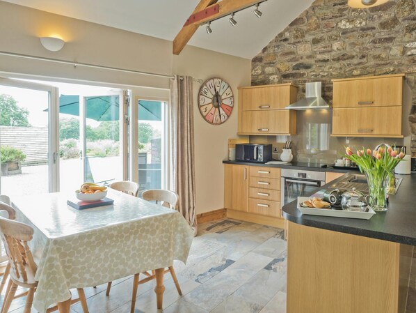 A kitchen with wooden cabinets, a microwave, a kettle, and a clock on the wall.