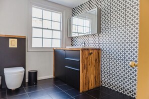 A modern bathroom with a large window, a wooden vanity, a black sink, and a patterned wall. - Beautiful Beachfront Townhouse (Saint Leonards)