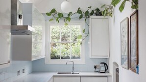 Una cuina moderna amb armaris blancs, un paviment amb dibuix negre i blanc, un finestral i una planta penjant.