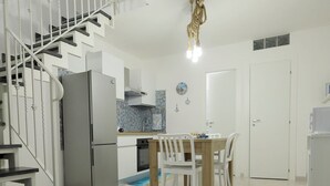 Eine moderne Küche mit Kühlschrank, Herd und Esstisch mit Stühlen. Eine Treppe mit Geländer führt zu einer oberen Ebene.