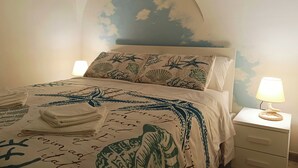 Ein Schlafzimmer mit einem Bett, das eine marine-inspirierte Bettdecke, einen dekorativen Kopfteil und zwei Nachttischlampen hat.