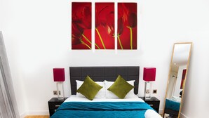 Una habitación de hotel con una cama, una mesita de noche, una lámpara, un espejo y obras de arte en la pared.