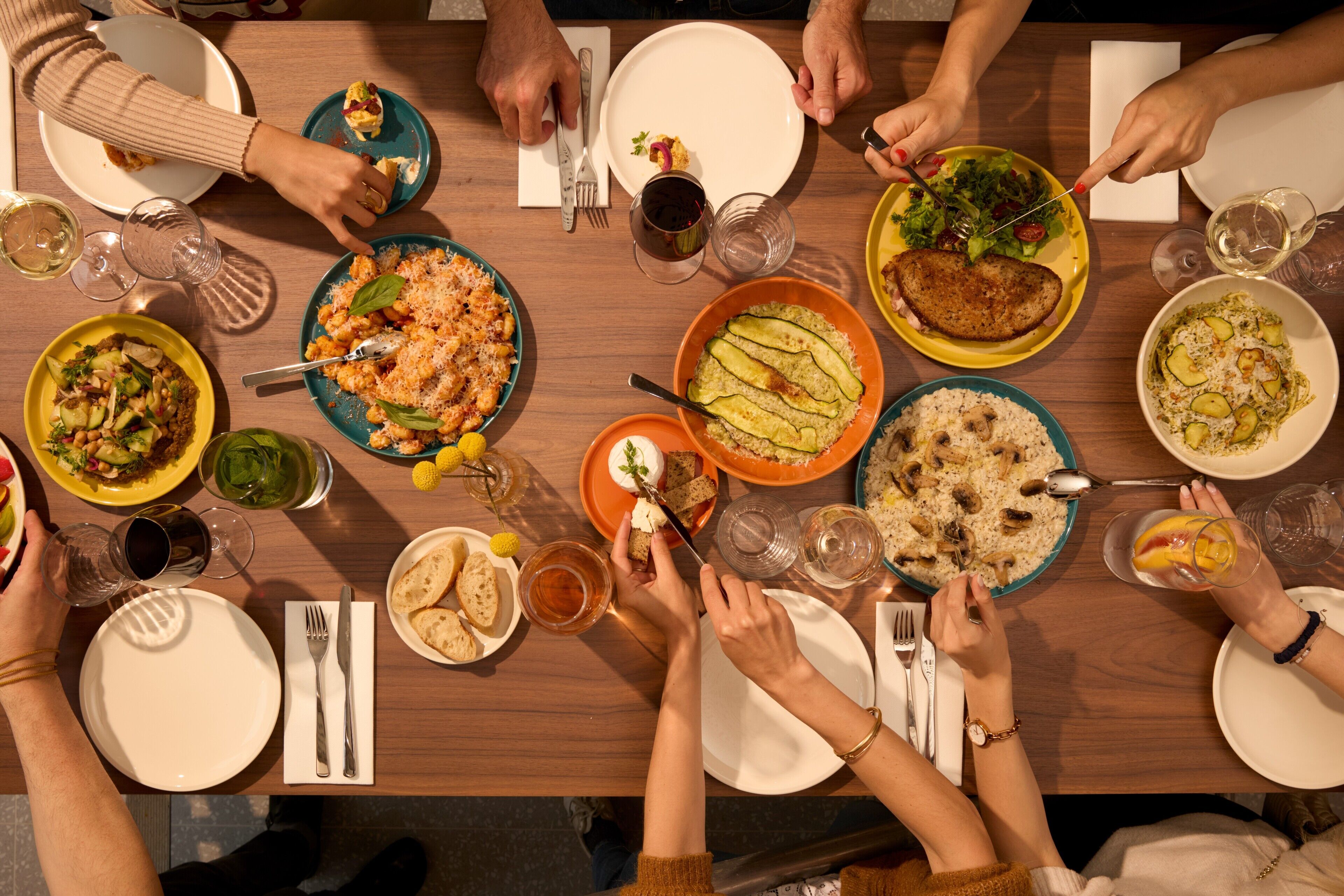 A group of people dining around a wooden table with various dishes and drinks.