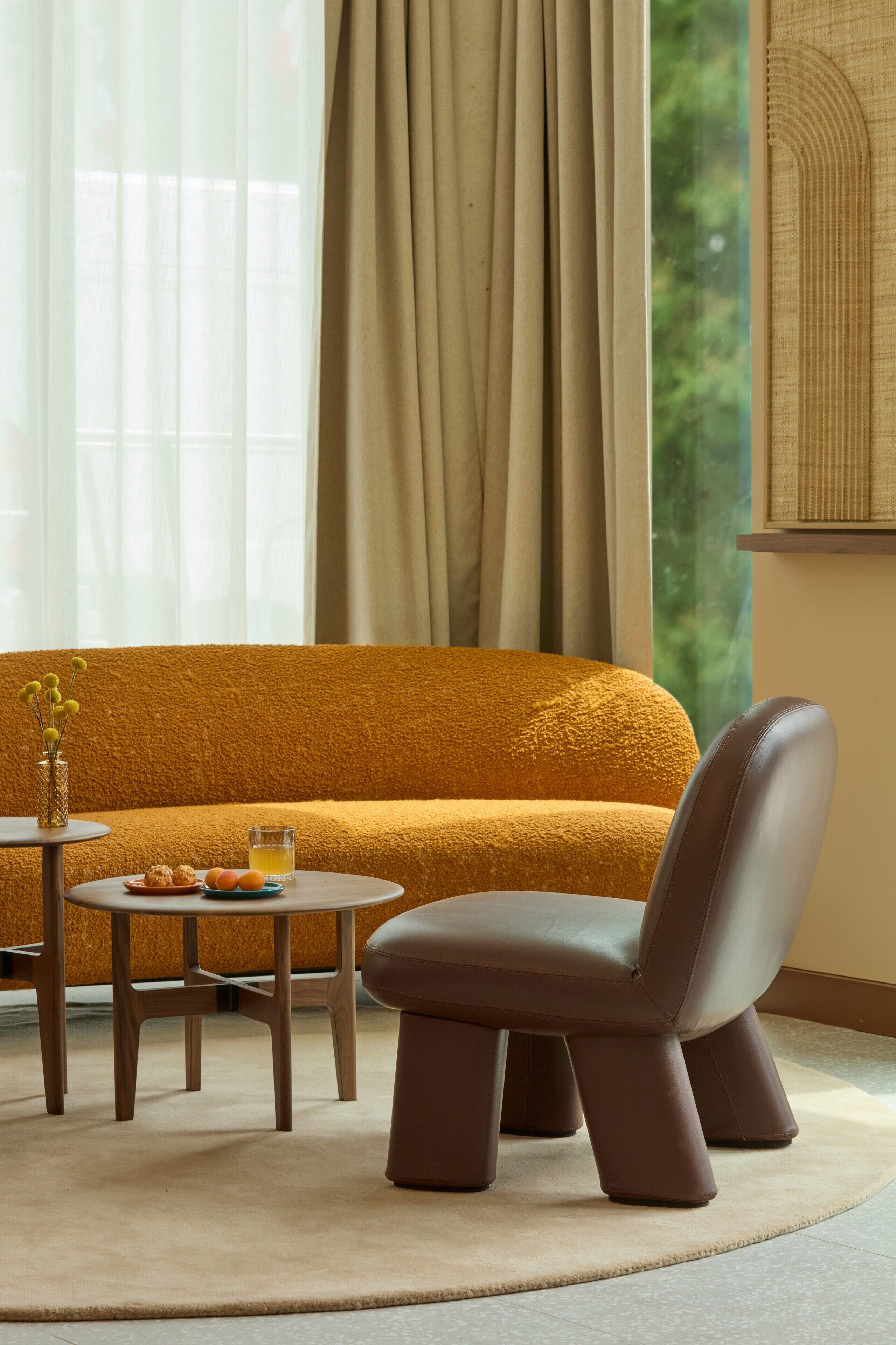 Uma sala de estar moderna com um sofá amarelo mostarda, uma poltrona de couro, uma mesinha redonda com um copo de suco de laranja e um vaso com flores amarelas.
