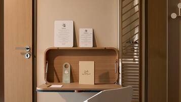 Une chambre d’hôtel moderne avec un bureau en bois, une chaise blanche et un miroir qui reflète un escalier.