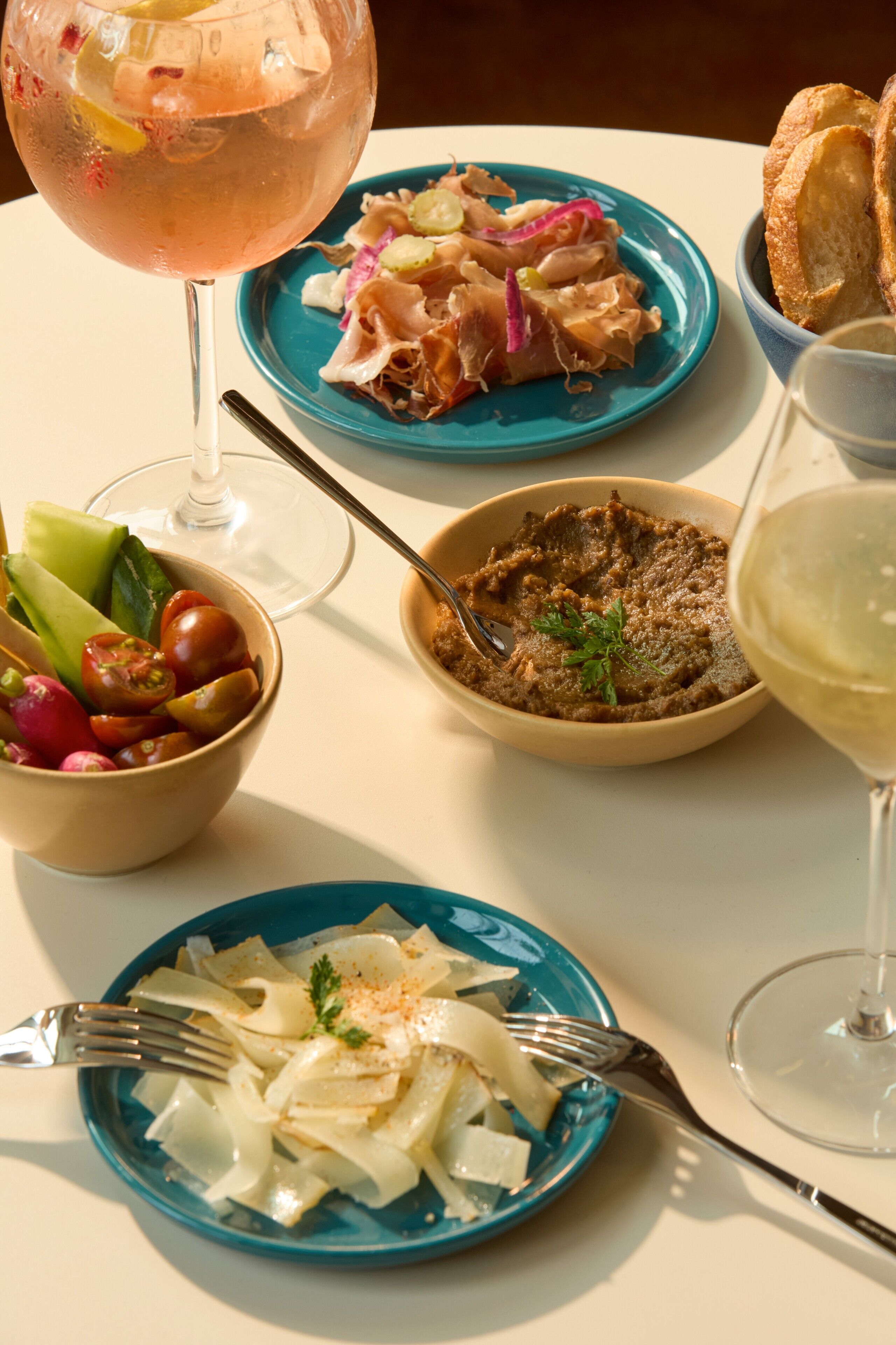 Een tafel met diverse gerechten, waaronder een portie pasta, een vleesschotel en een glas wijn.