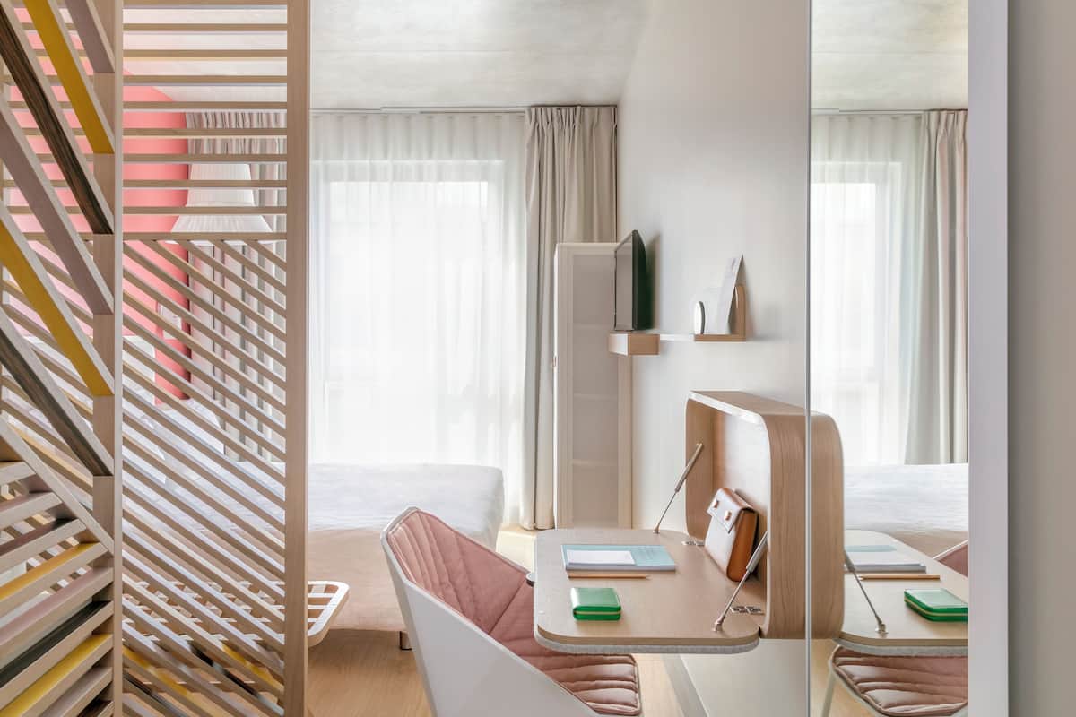 Een moderne hotelkamer met een bed, een bureau met stoel, een spiegel en een raam met gordijnen.