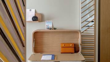 Een moderne, minimalistische kamer met een wand met een geometrisch patroon, een houten bureau met een laptop, een notitieboekje en een pen, en een witte stoel.