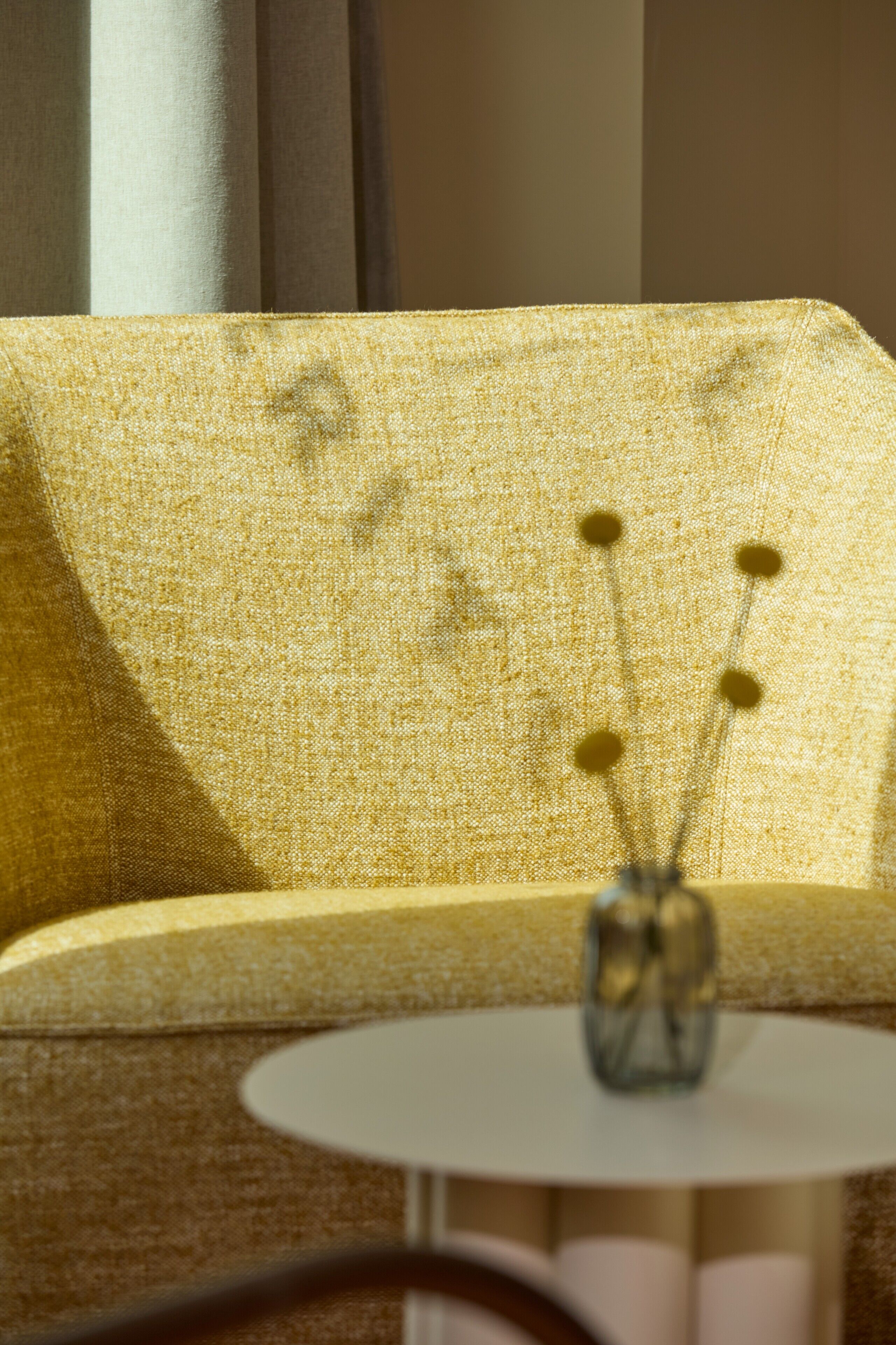 A yellow sofa with a vase of yellow flowers on a small round table.