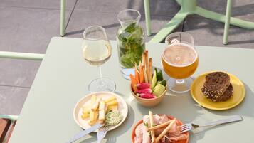 Una mesa servida con comida y bebidas, incluyendo un plato de queso, un bol de fruta y una jarra de cerveza.