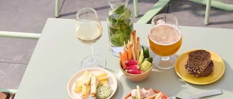 Una mesa servida con comida y bebidas, incluyendo un plato de queso, un bol de fruta y una jarra de cerveza.
