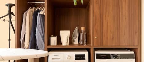 A laundry area with two washing machines, a drying rack, and shelves with towels and plants.