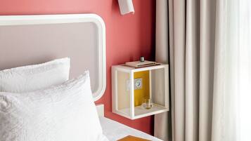 Ein ordentlich bezogenes Bett mit weißen Leinen, ein weißer Kopfteil und ein Nachttisch mit Lampe und kleiner Ablagefläche.