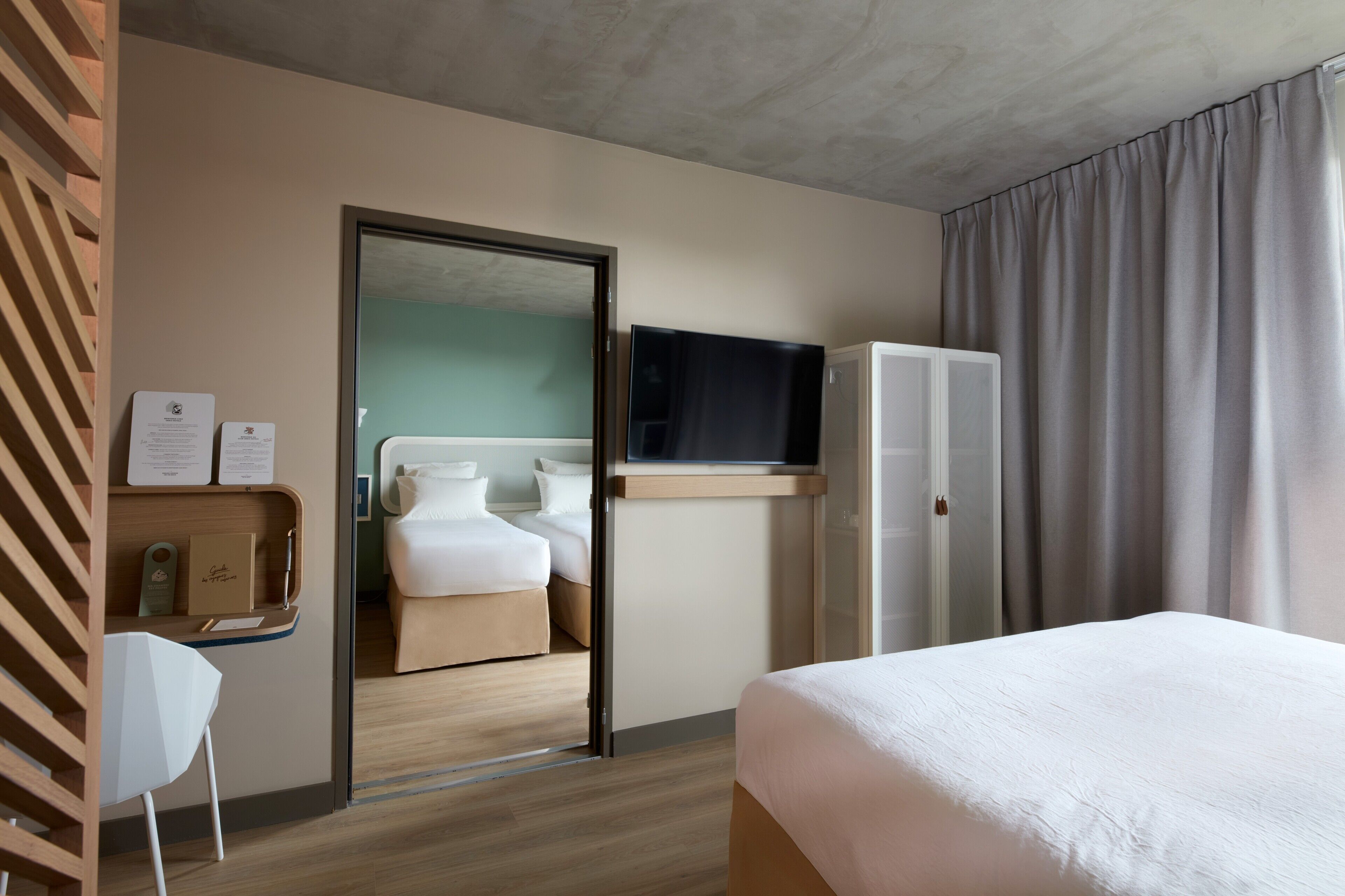 Une chambre d’hôtel moderne équipée d’un lit, d’un téléviseur fixé au mur, d’un bureau avec une chaise et d’une porte donnant sur une autre pièce.