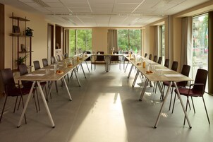 Un salón de conferencias con una larga mesa, sillas y vistas a árboles a través de grandes ventanales.