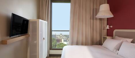 A hotel room with a bed, a television, a wardrobe, a window with curtains, and a bedside lamp.