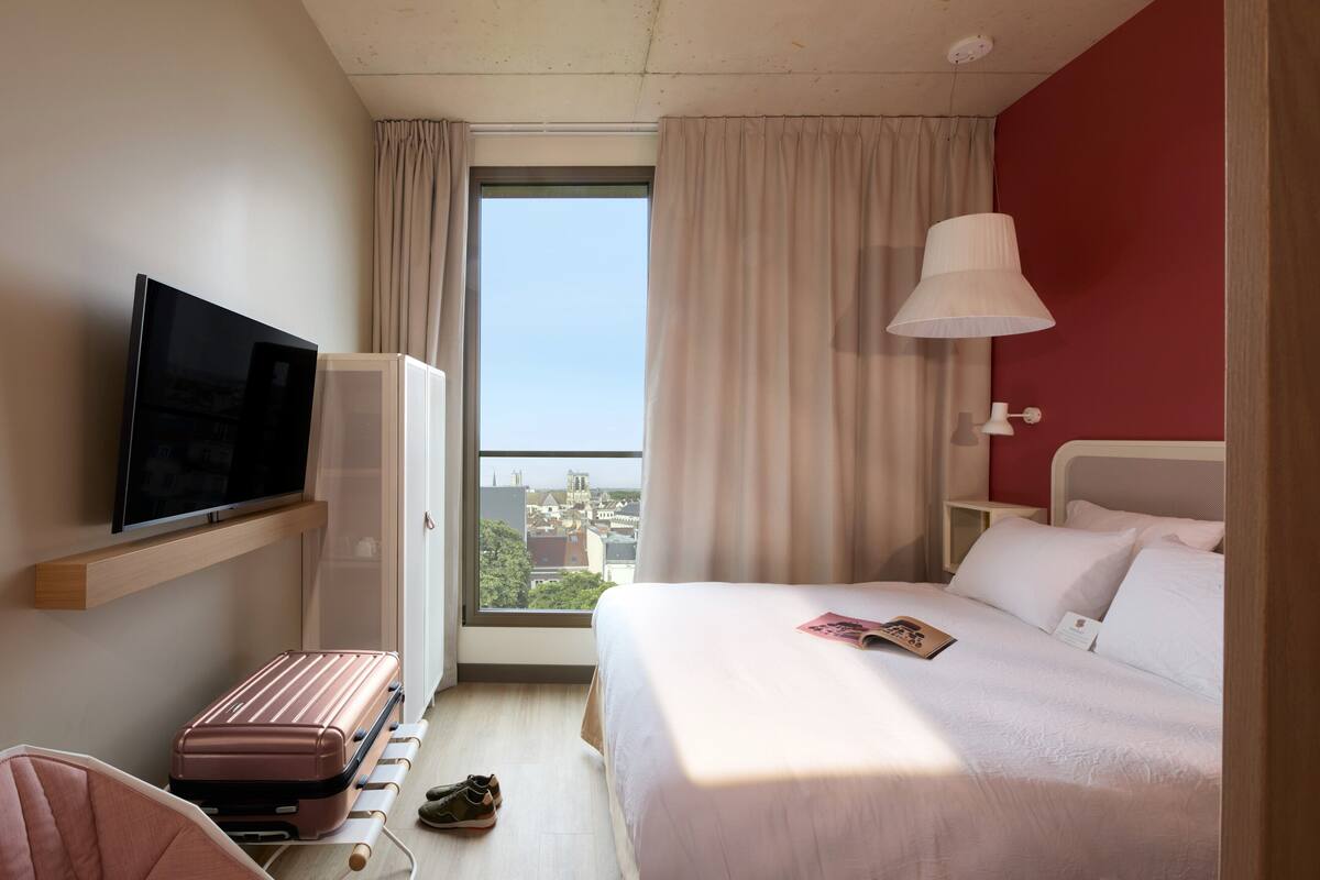 Hotelkamer met een bed, televisie, koffer en raam met gordijnen.
