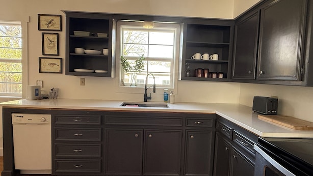 A modern kitchen with dark cabinetry, a built-in dishwasher, and a window providing natural light. - Ideal location close to Texas Tech, University Medical Center, Covenant Hospital (Lubbock)