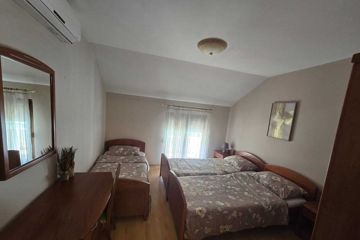 Une chambre avec deux lits, un bureau, un miroir, un luminaire au plafond et une fenêtre avec des rideaux.