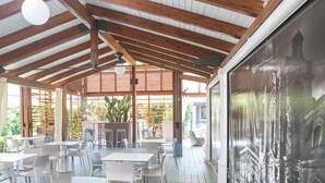 Un espace de restauration intérieur avec des tables et des chaises blanches, des poutres en bois au plafond et une grande fresque sur le mur de droite.
