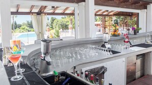 Un espace bar avec vue sur la piscine, des ustensiles de bar, ainsi qu’un assortiment de verres et de bouteilles.