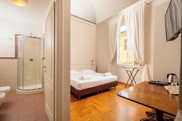 Habitación de hotel con ducha, cama, suelo de madera y una mesa con tetera y vasos.