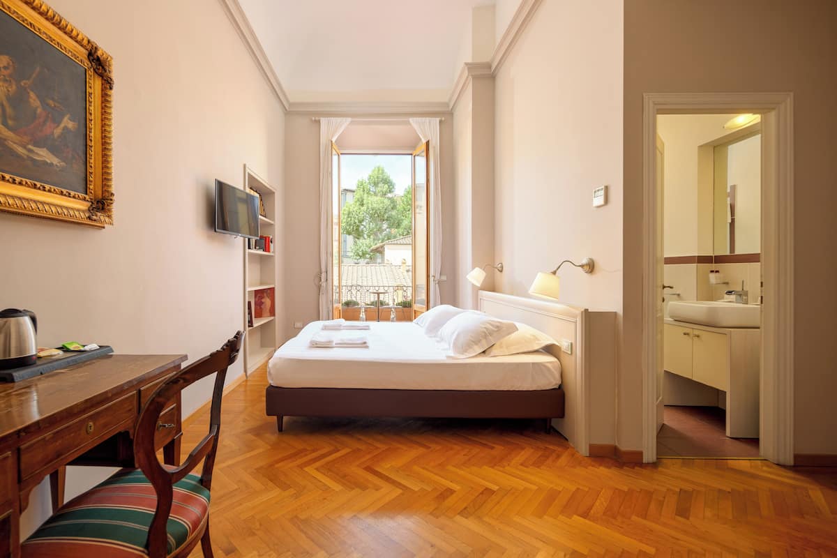 A hotel room with a bed, a desk with a chair, a television, and a view of the outside.