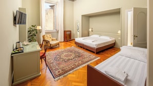 Habitación de hotel con una cama grande, una cama más pequeña, un escritorio con silla, un espejo y una ventana con cortinas.