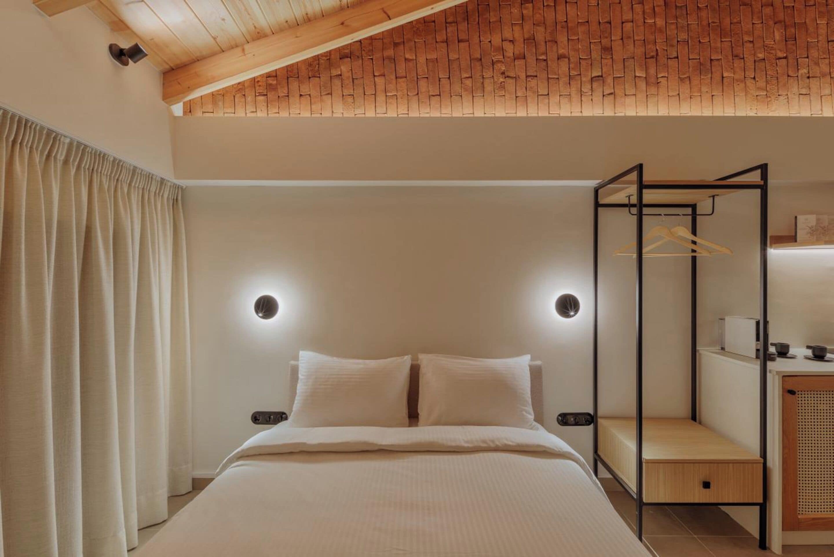 Un dormitorio con cama, techo de madera, lámpara de pared, perchero y una mesita de noche pequeña.