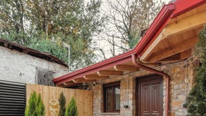 Un edificio de piedra con techo rojo, una puerta de madera y un sendero de piedra que conduce a un pequeño jardín con plantas en macetas y una fuente de piedra.