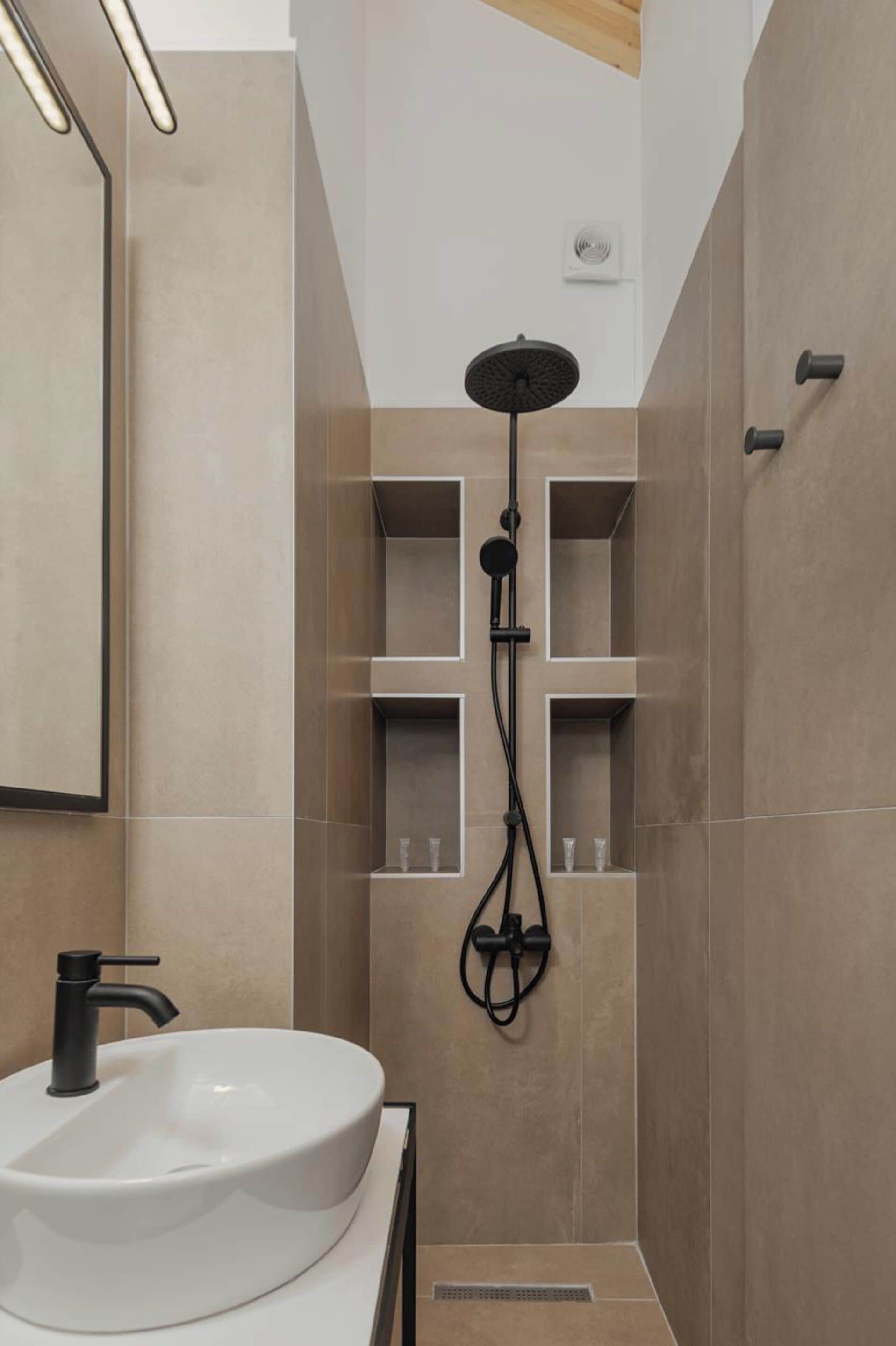 Une salle de bain moderne avec un lavabo blanc, un robinet noir, une douche avec un pommeau noir et un miroir au mur.