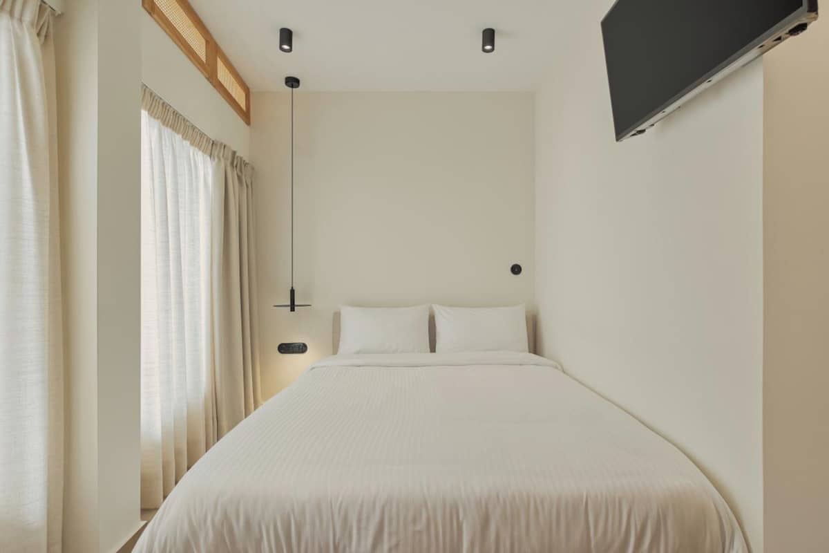 Quarto com cama, cortinas, televisão na parede e abajur.