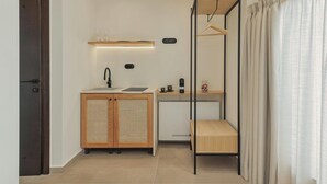 Una habitación pequeña con kitchenette, un armario de madera, una percha y una ventana con cortinas.