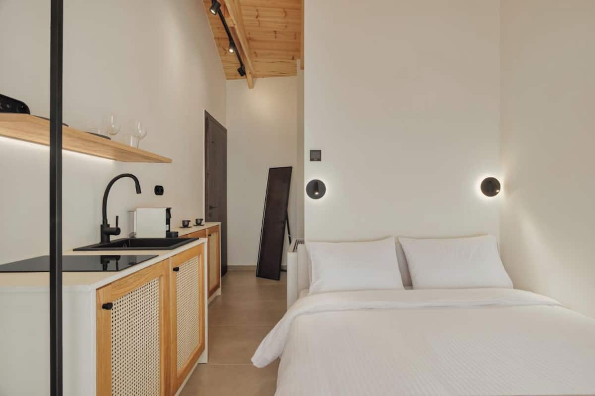Quarto de hotel moderno com cama, cozinha compacta e teto de madeira.