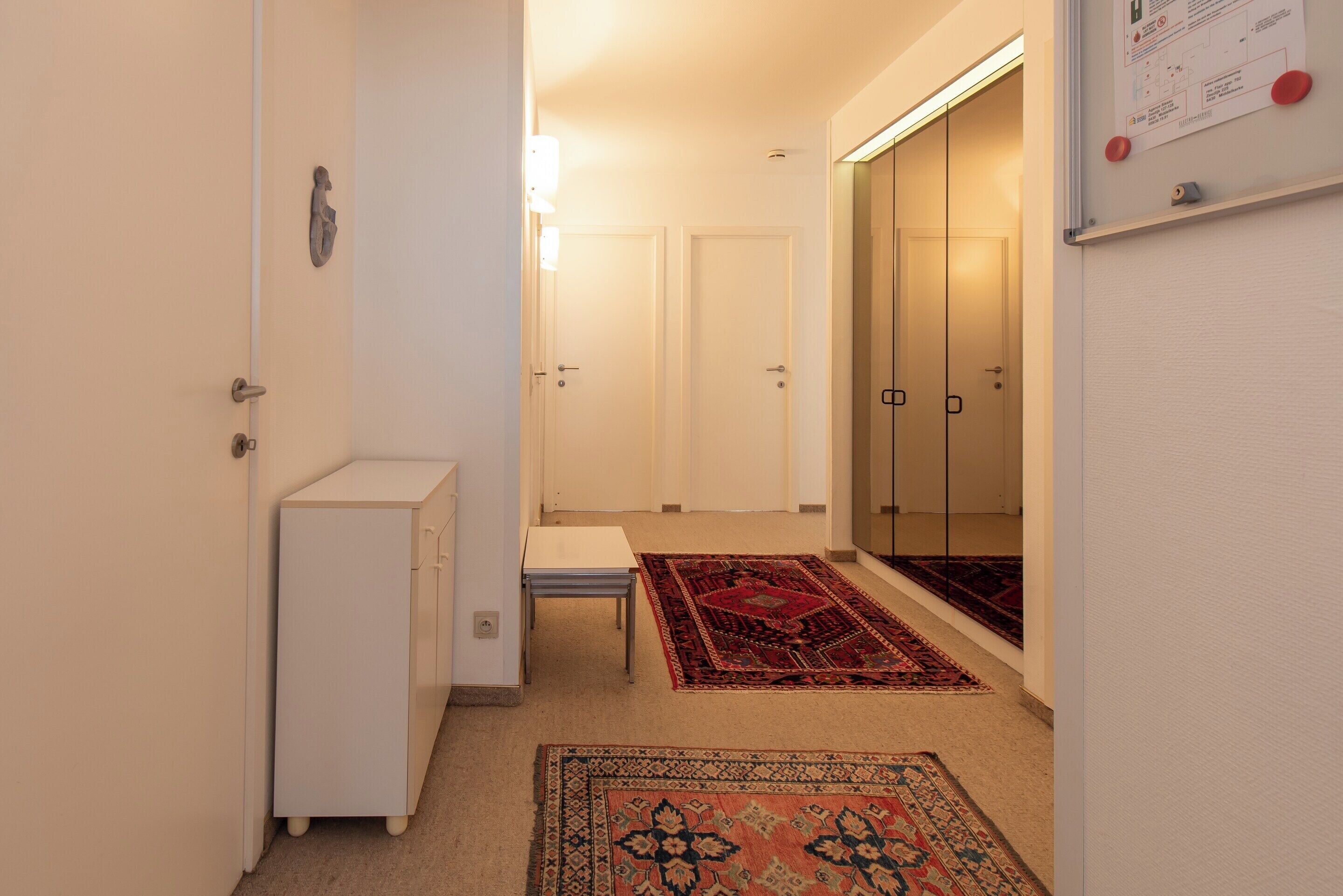 Un couloir avec une armoire blanche, une petite table et deux portes donnant sur une pièce.